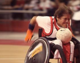 Wheelchair woman struggling to carry rugby ball