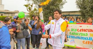 Portador de la antorcha posa sonriente frente a una banderola a favor de las personas con discapacidad en el tercer día del Relevo de la Antorcha Parapanamericana de Lima 2019