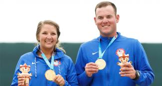 Ashley Carroll y Derek Haldeman sosteniendo con en una mano la Medalla de Oro y con la otra una artesanía de Milco, en los Juegos Lima 2019