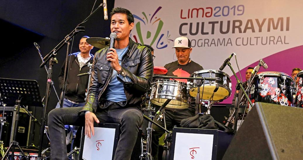 Artista Tony Succar sentado con micrófono en show musical del Culturaymi del 4 de agosto en Lima 2019