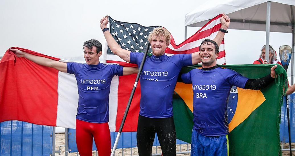 Itzel Delgado de Perú, Connor Baxter de EEUU y Vinicius Martins de Brasil celebran juntos haber obtenido medallas en la competencia de Surf SUP masculino en los Juegos Lima 2019, en Punta Rocas.