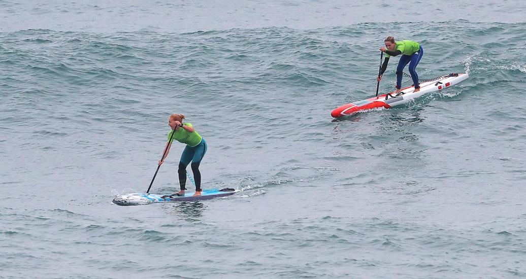 Two surfers are sliding on their boards in the women’s SUP surfing final in Punta Rocas.